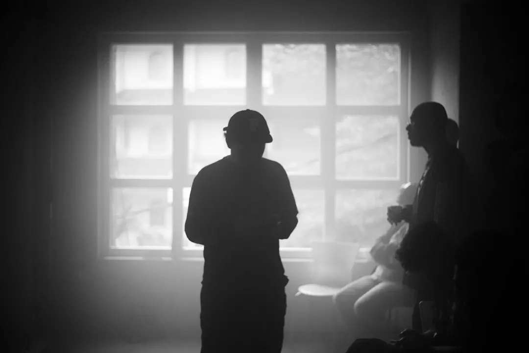 Two figures stand silhouetted against a window